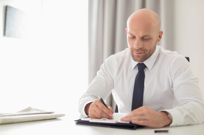 Mid adult businessman writing on clipboard in home office